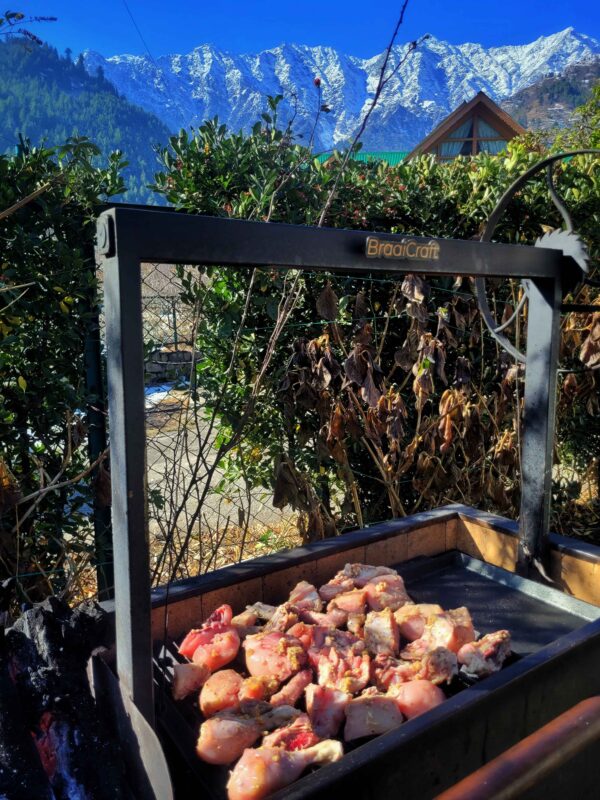 Stoker grilling chicken asado at BraaiCraft Smokehouse with snowcapped mountains at the backdrop